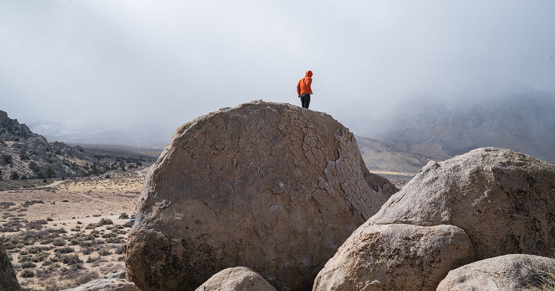 person in orange jacket standing on large stones