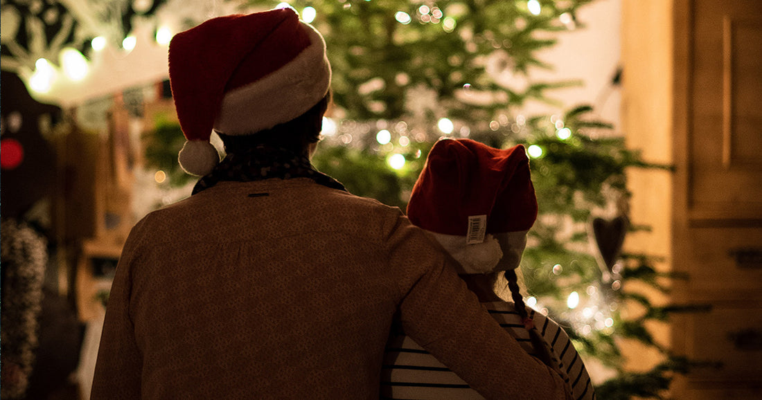 father and daughter wearing santa hats in from on lit up Christmas tree