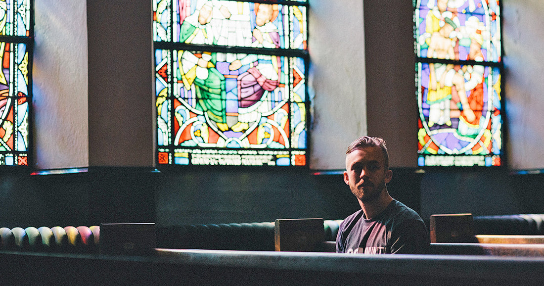 man sitting in dark church backlit by colorful stained glass windows