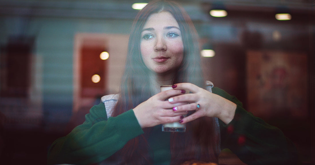woman in green sweater sitting comfortably inside with hot beverage