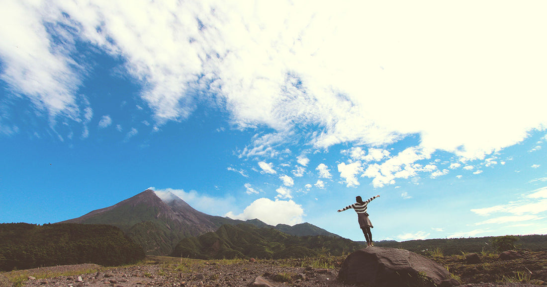 woman holds out arms and looks up at blue sky and mountain