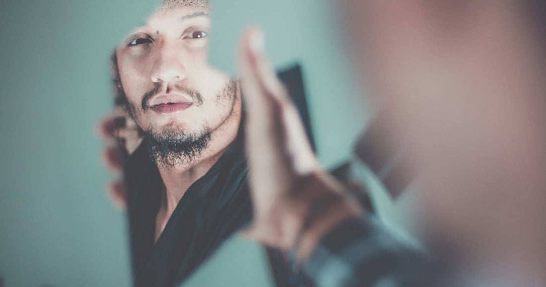man holds broken mirror with reflection of his face