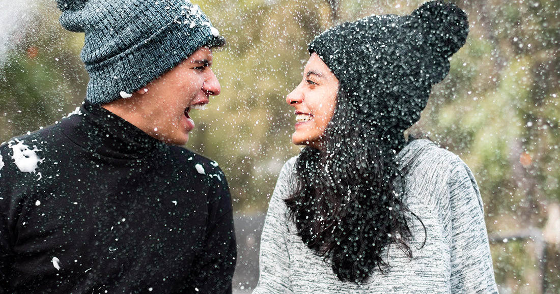 two people smiling at each other during snowfall