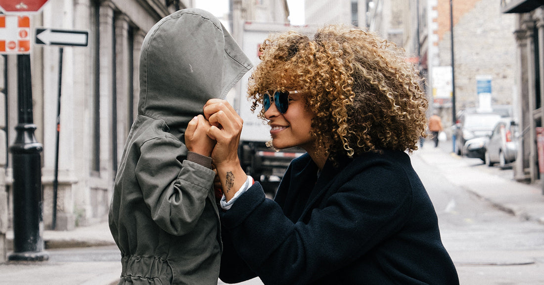 mom wearing glasses gets down on knee to talk to kid in jumpsuit