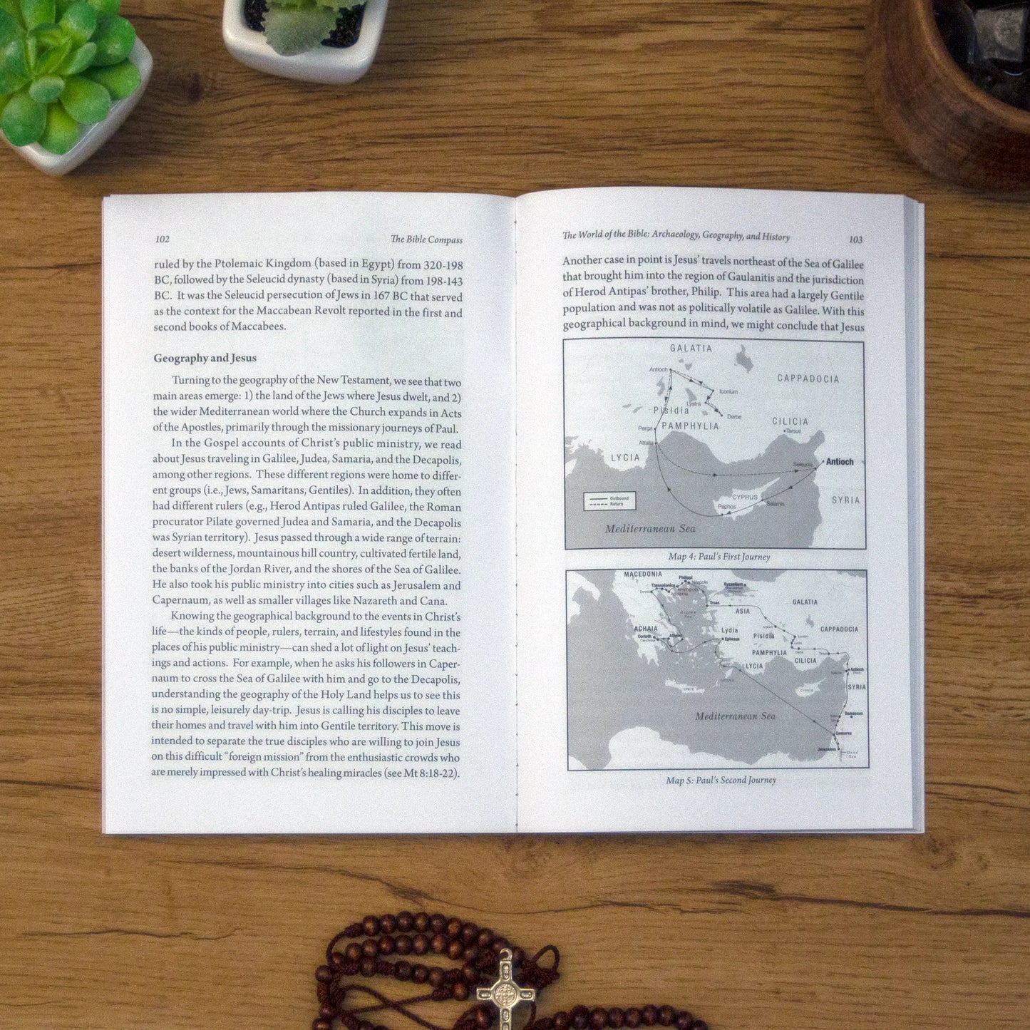 A tabletop lifestyle shot of the catholic book, The Bible Compass: A Catholic's Guide to Navigating the Scriptures by Edward Sri published by Ascension, laying open on a wooden table.