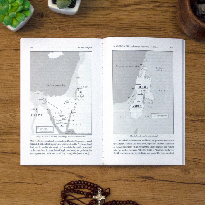 A tabletop lifestyle shot of the catholic book, The Bible Compass: A Catholic's Guide to Navigating the Scriptures by Edward Sri published by Ascension, laying open on a wooden table. The pages feature maps.