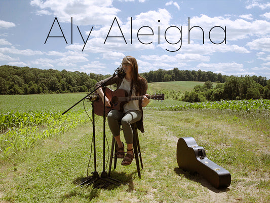 Aly Aleigha playing guitar in field with blue skies