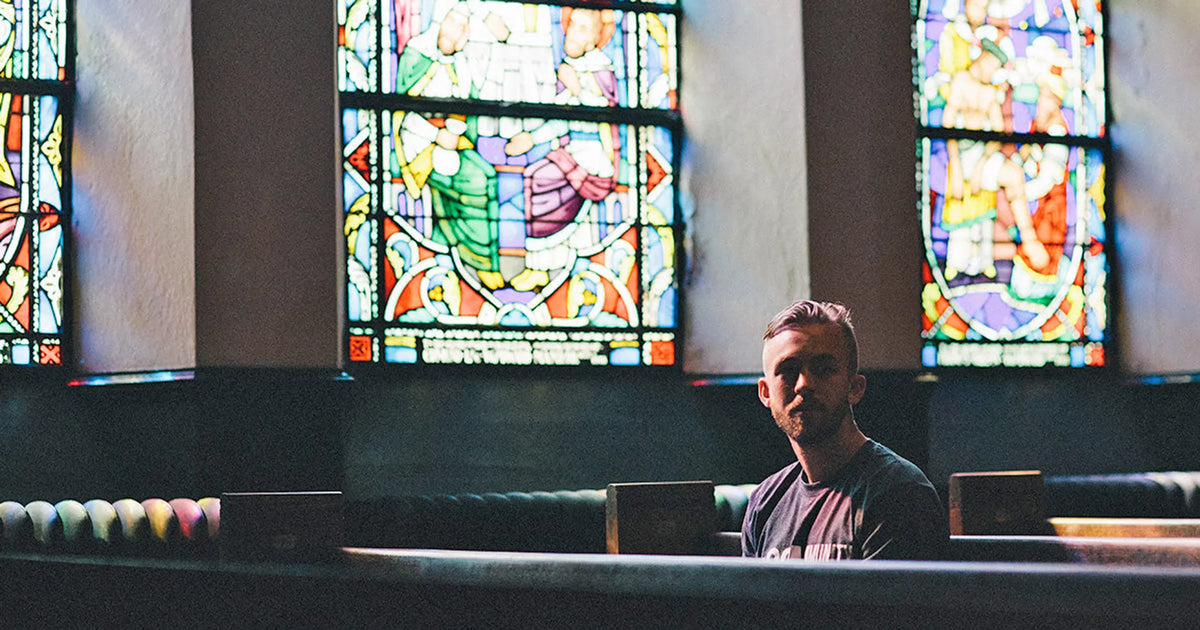 man sitting in dark church backlit by colorful stained glass windows