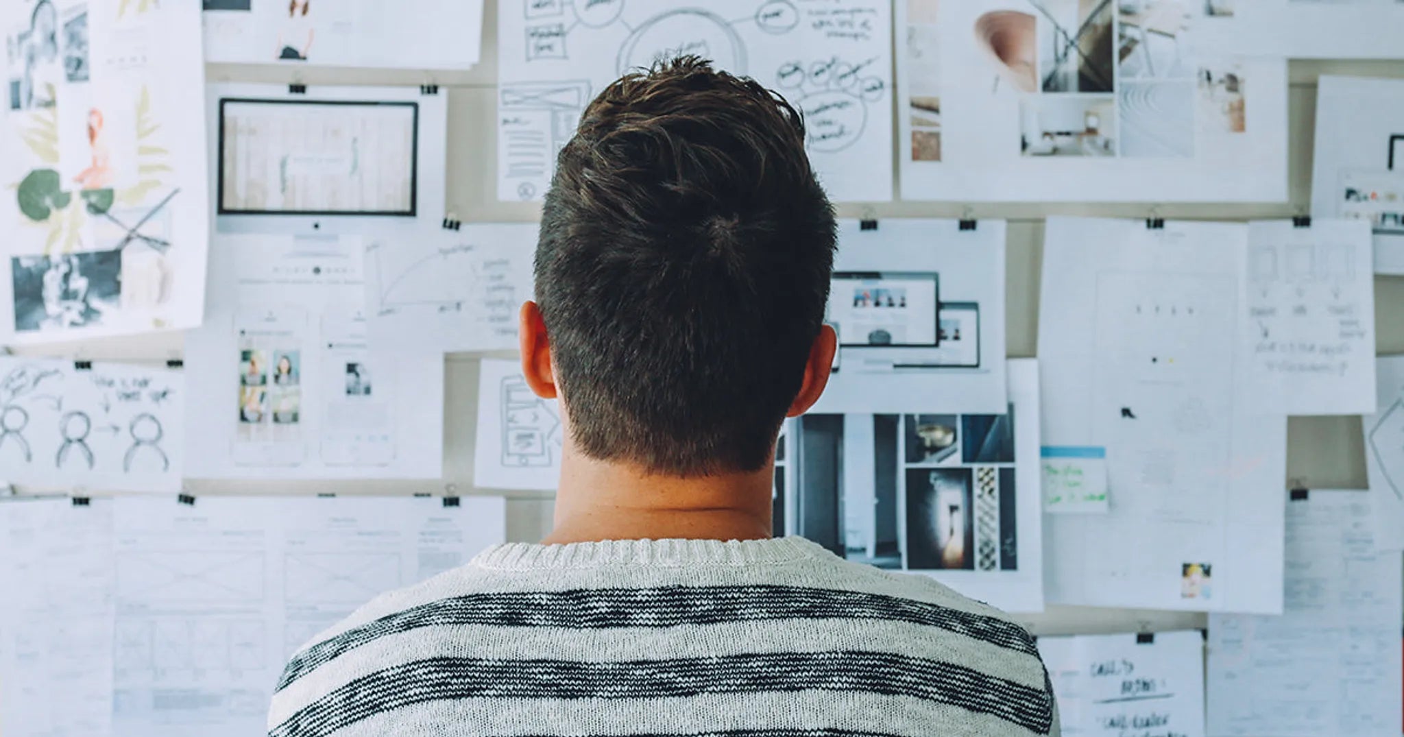 man looks at wall with different graphs and papers