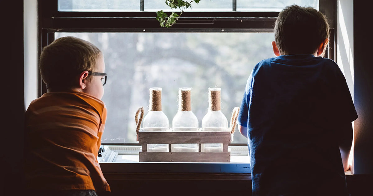 two kids looking out a window near glass bottles