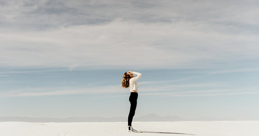 woman in white shirt standing on sand looking up