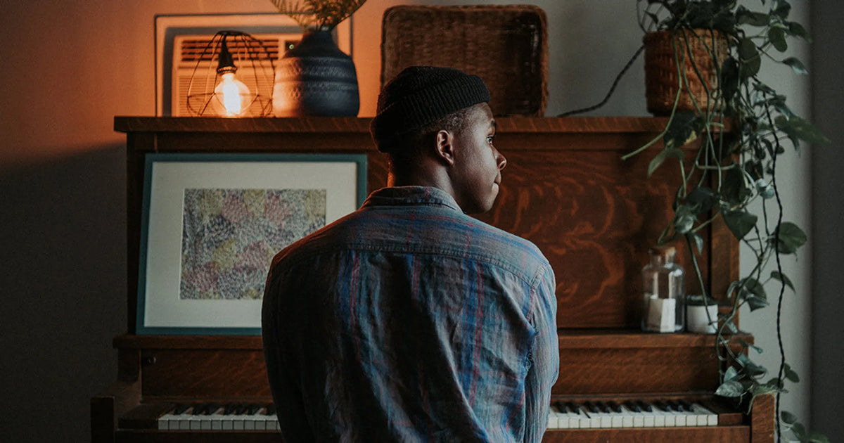 man sitting at piano with potted plant and picture frame