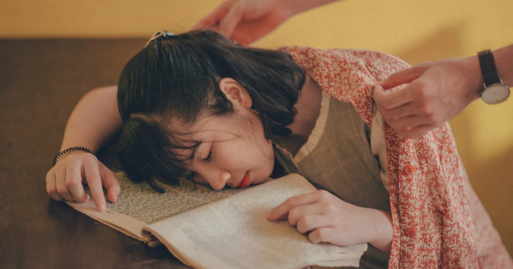 person places red checkered blanket on woman asleep at desk