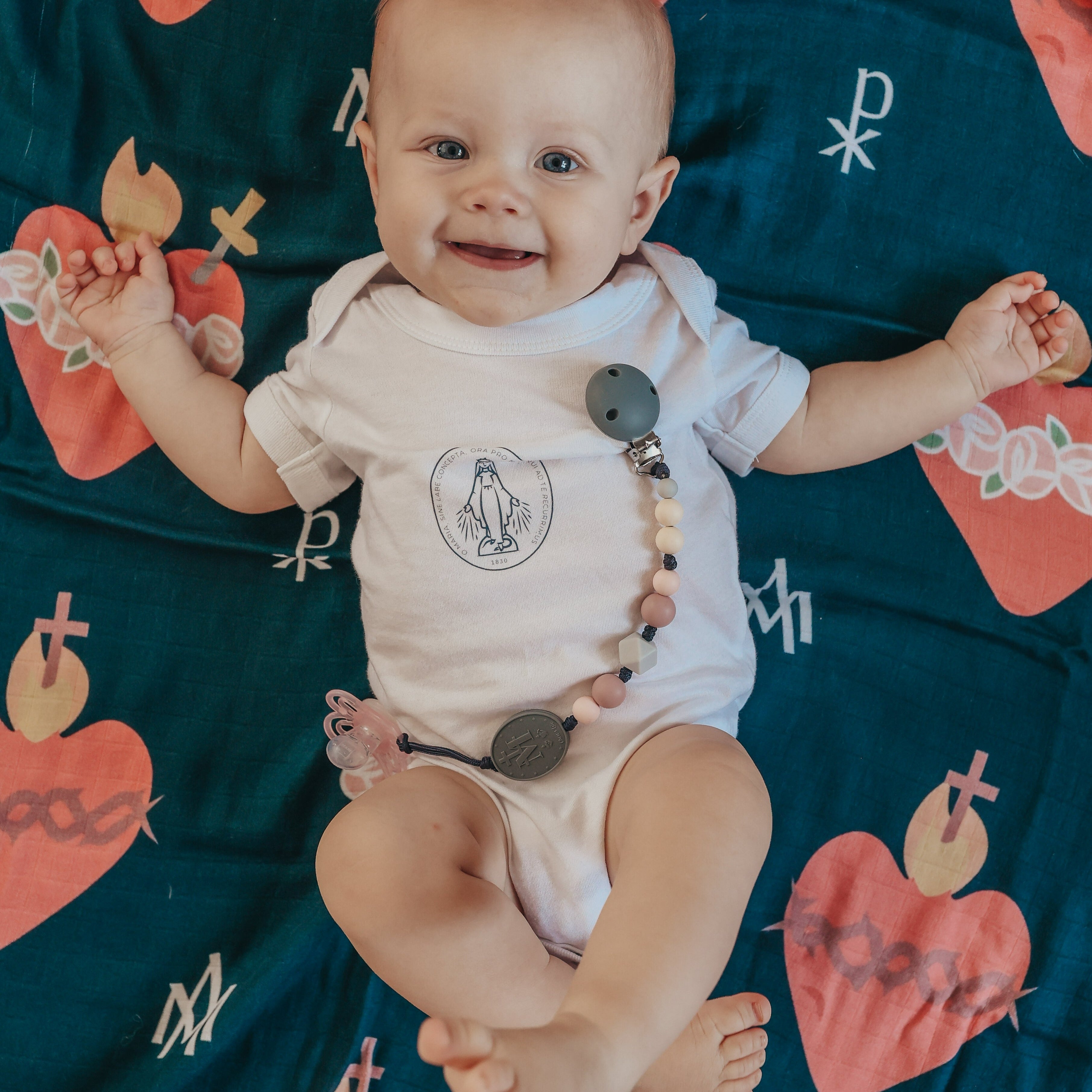 Baby wearing a white onesie with a graphic design, sitting on a colorful blanket.