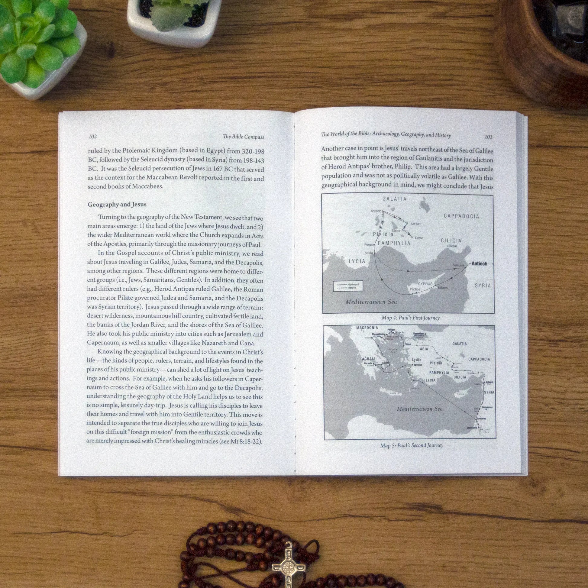 A tabletop lifestyle shot of the catholic book, The Bible Compass: A Catholic's Guide to Navigating the Scriptures by Edward Sri published by Ascension, laying open on a wooden table. 