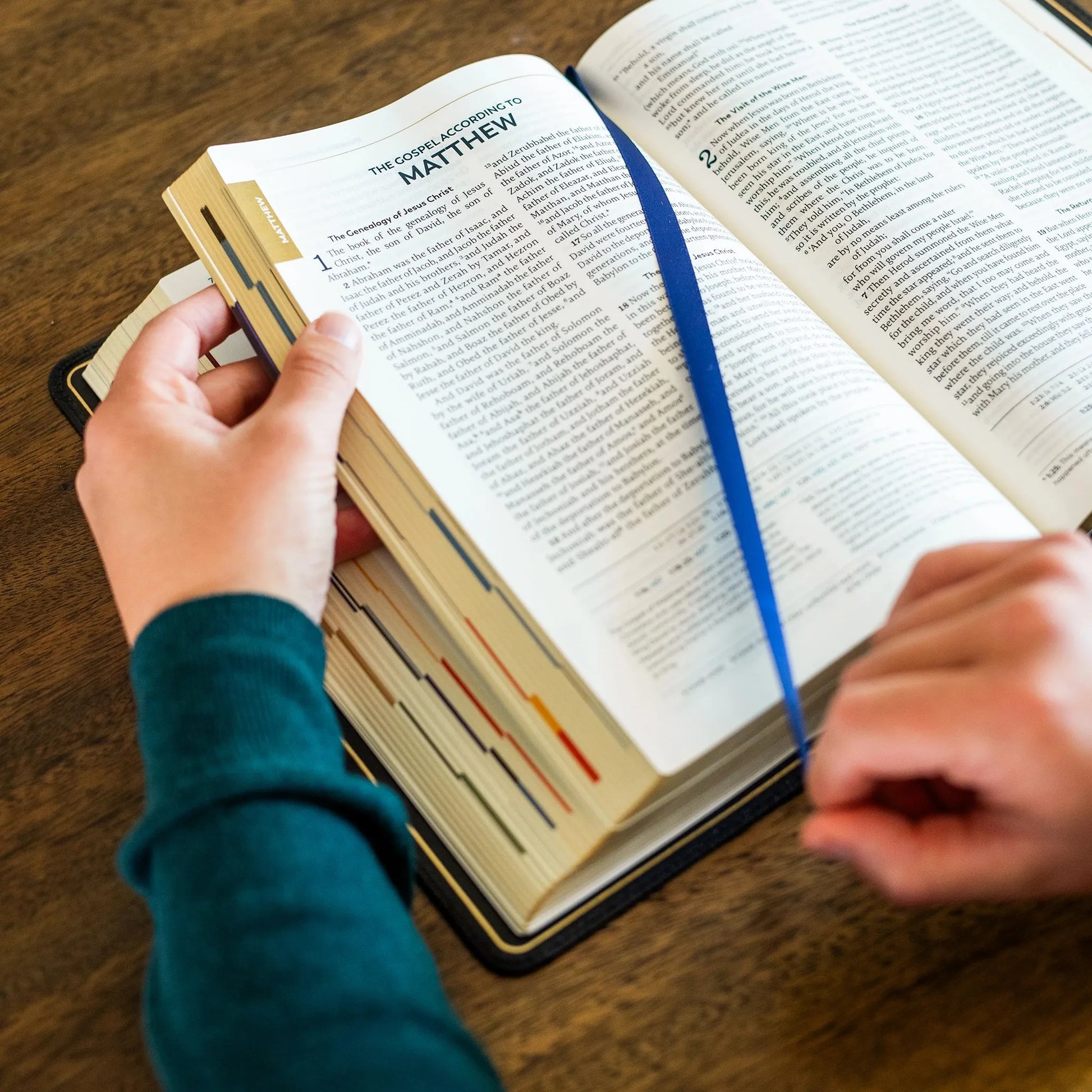 Open Bible with a hand turning the page on a wooden surface
