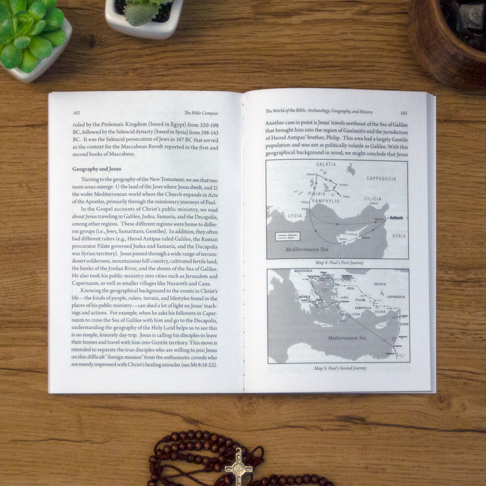 A tabletop lifestyle shot of the catholic book, The Bible Compass: A Catholic's Guide to Navigating the Scriptures by Edward Sri published by Ascension, laying open on a wooden table. 
